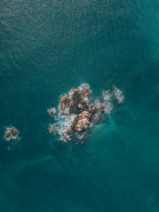 An aerial view of the ocean with rocks in the water