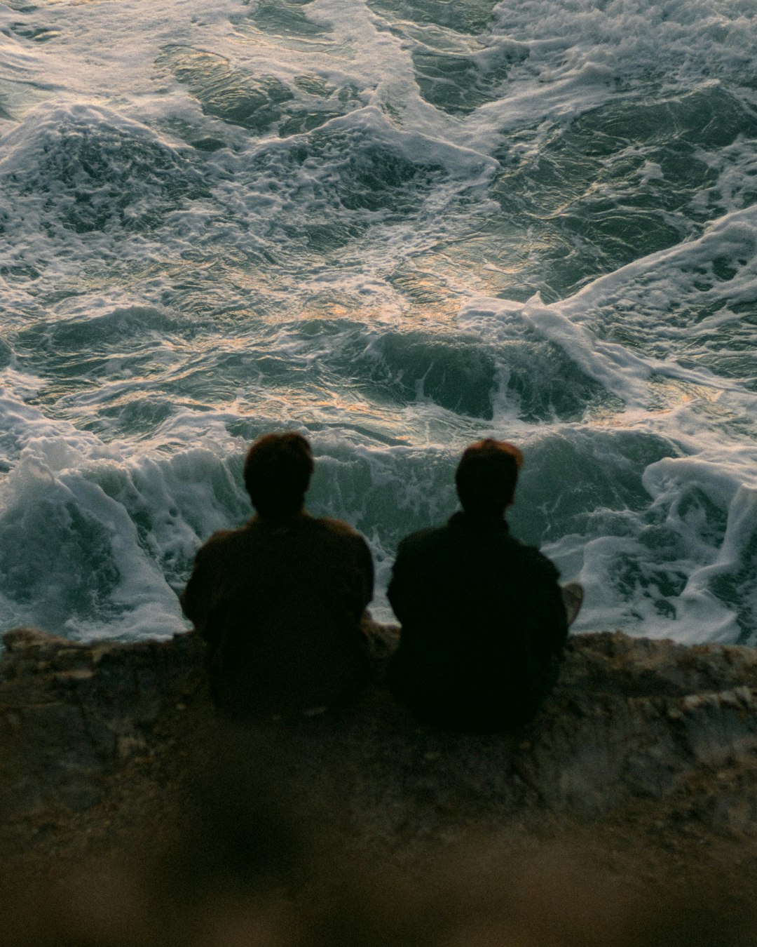 Two people sitting on a rock looking out at the ocean