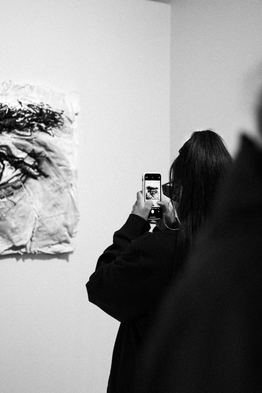 A woman taking a picture of a painting on a wall