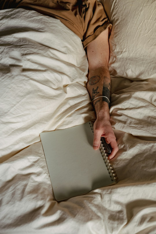 A person laying in bed with a notebook in their hand