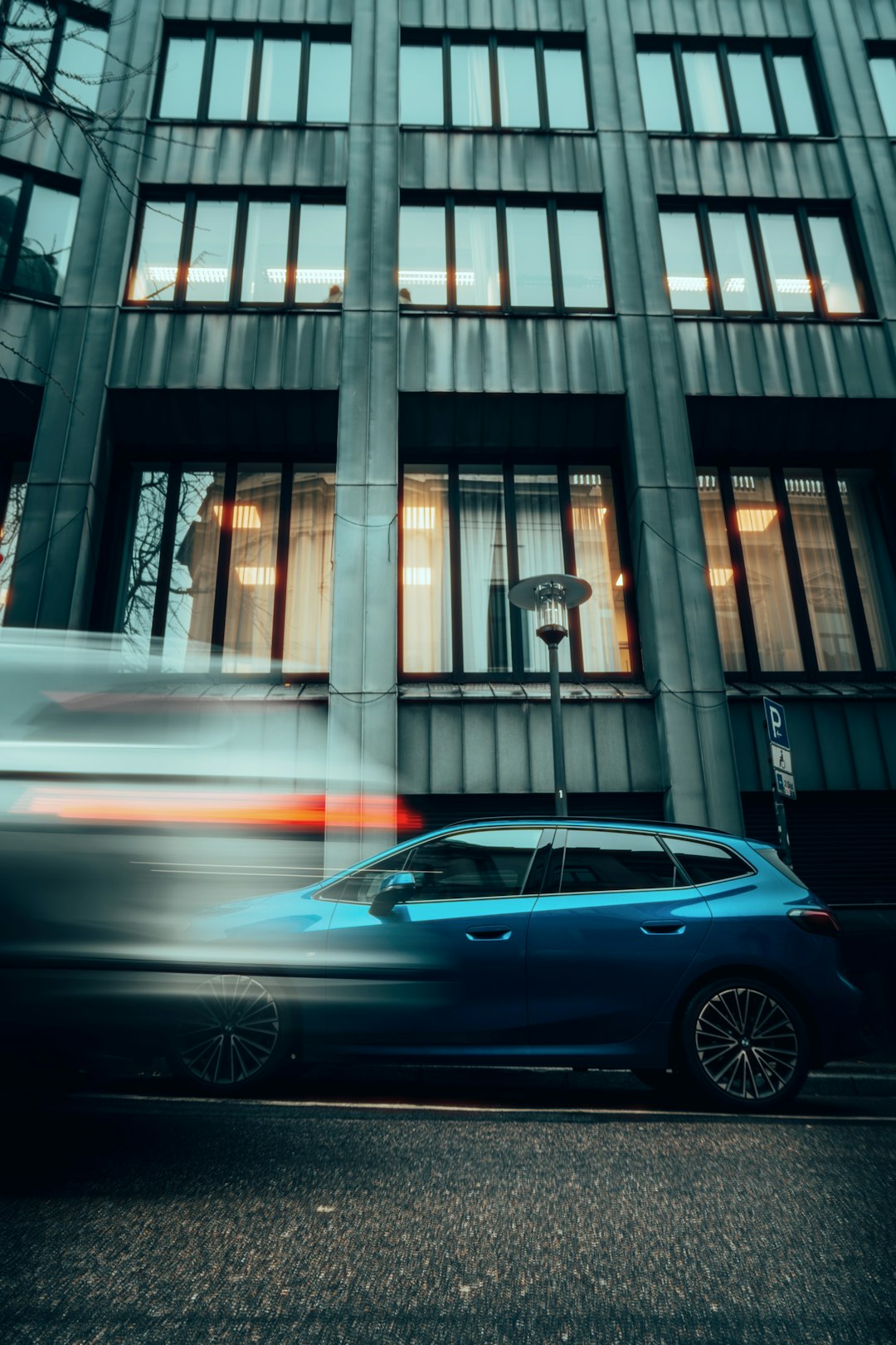 A blue car driving past a tall building