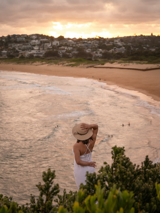 A woman in a white dress and hat standing on a beach