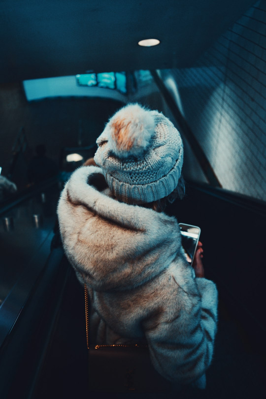 A person riding an escalator wearing a hat and coat