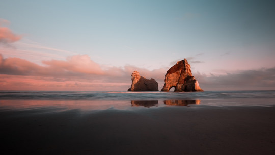 A large rock sitting on top of a beach next to the ocean