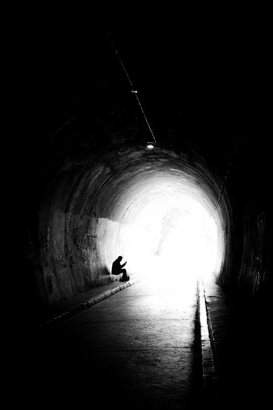 A person sitting in the middle of a dark tunnel