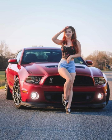 Mujer posando frente a un mustang rojo