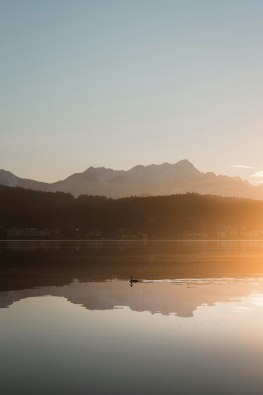 The sun is setting over a lake with mountains in the background