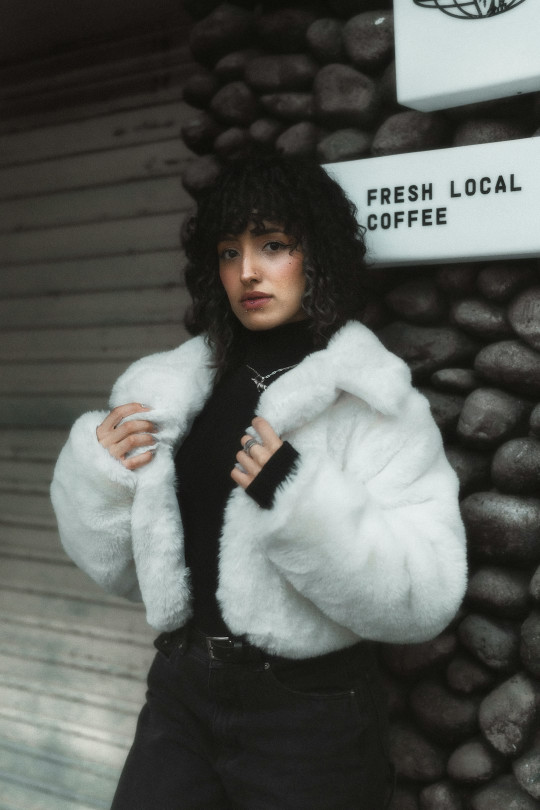 A woman in a white fur coat leaning against a wall