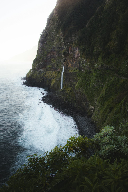 A waterfall on the side of a cliff next to the ocean