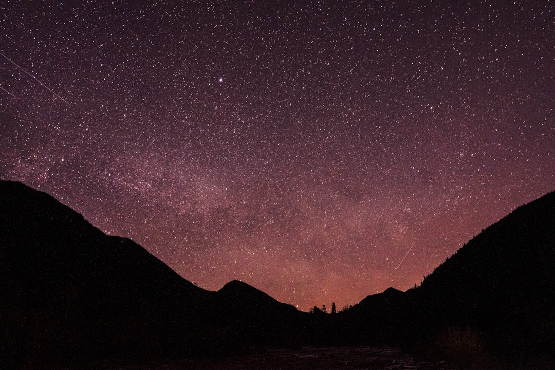 The night sky is filled with stars above a mountain range