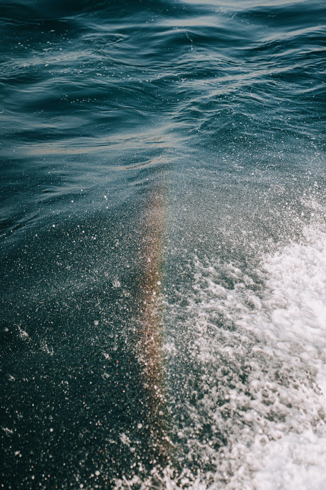 A rainbow is seen in the water from a boat