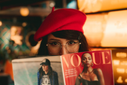 A woman in a red hat is reading a magazine