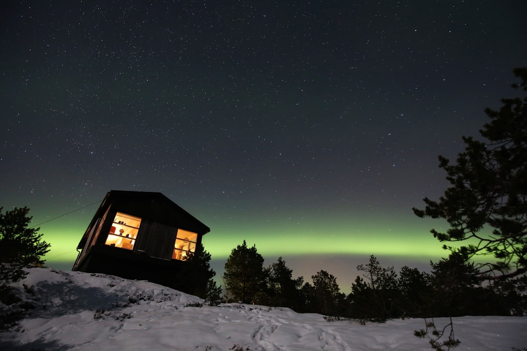 A cabin in the snow with a green aurora light in the background