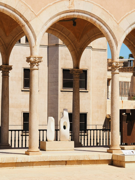 A large building with arches and sculptures in front of it