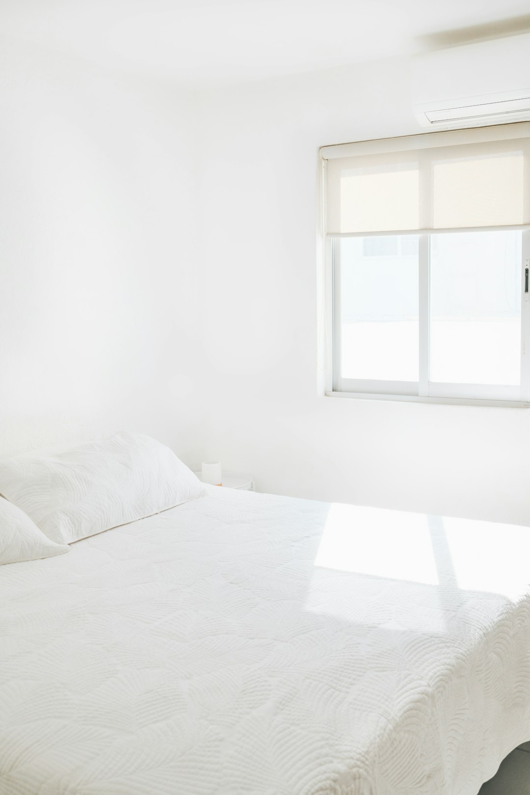 A clean, white bedroom with bright sunlight.