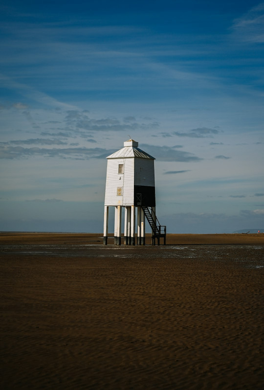 A lighthouse stands on a sandy beach.