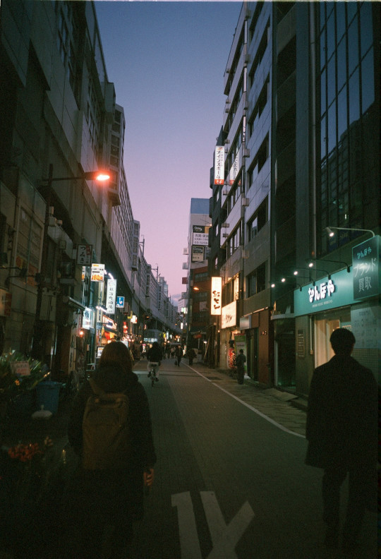 A couple of people walking down a street next to tall buildings