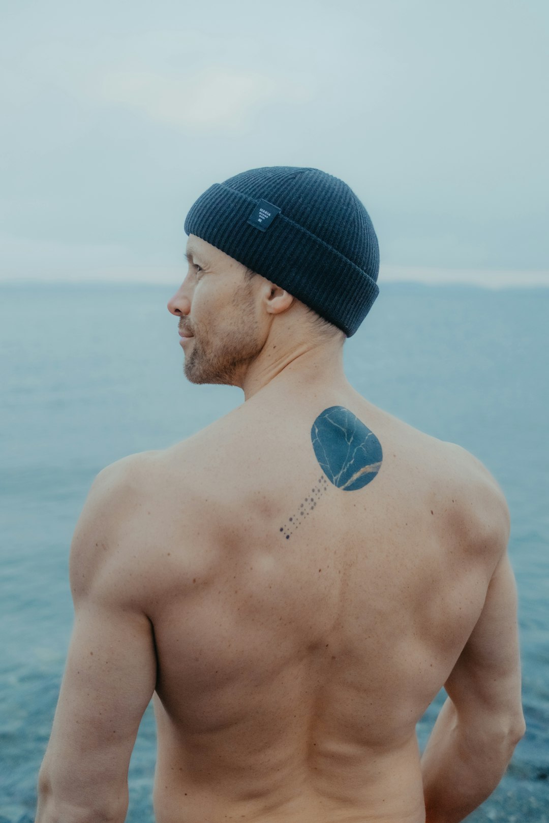 A man with a tattoo on his back standing next to the ocean