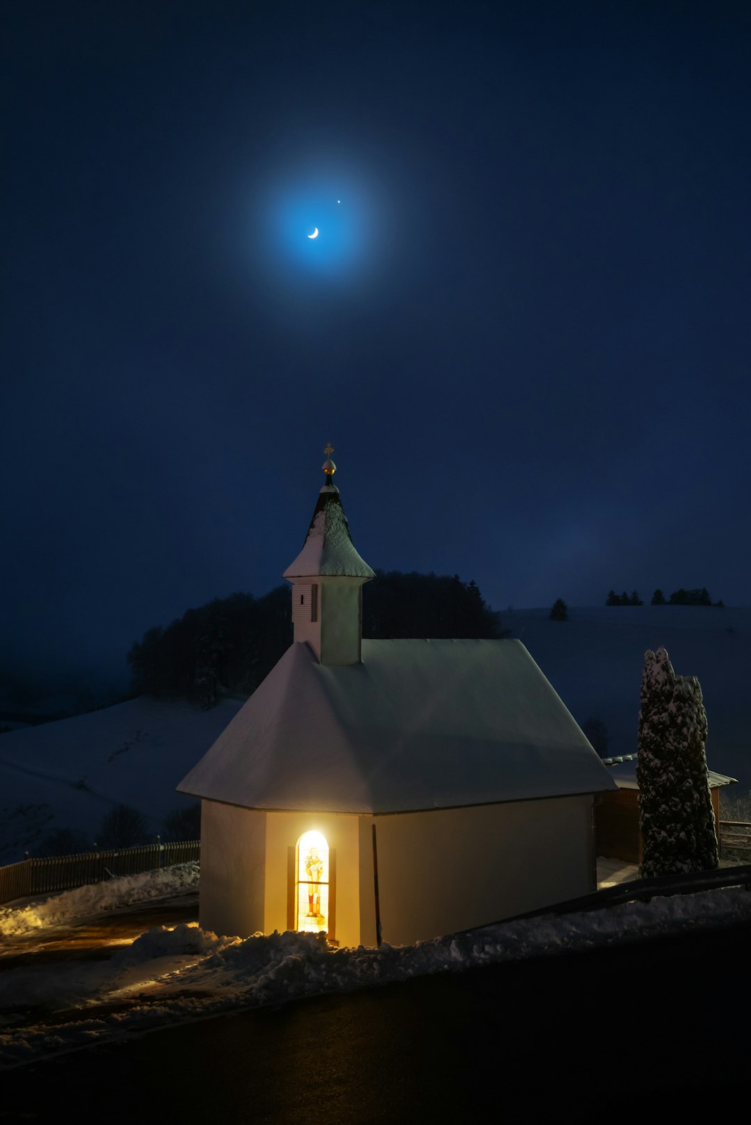 A church in the snow at night with the moon in the sky