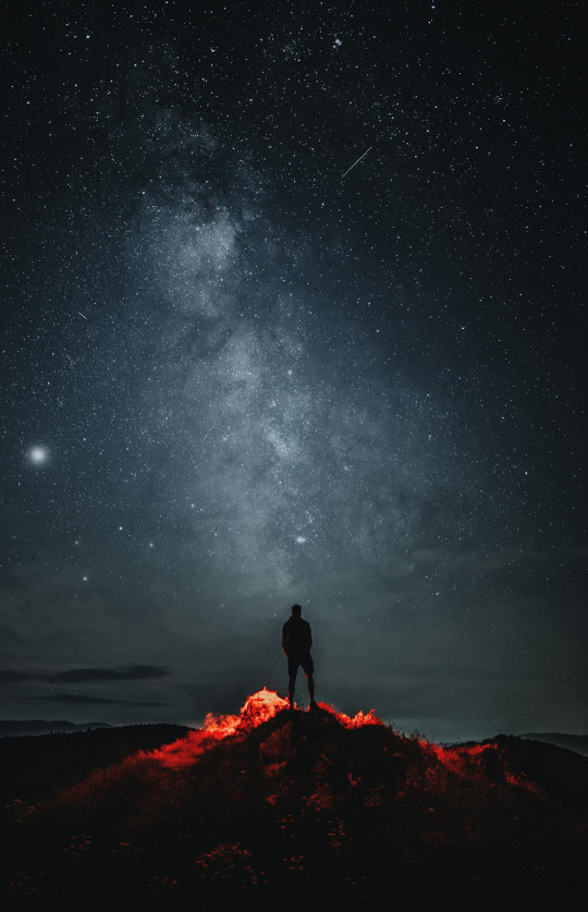 A man standing on top of a mountain under a night sky filled with stars