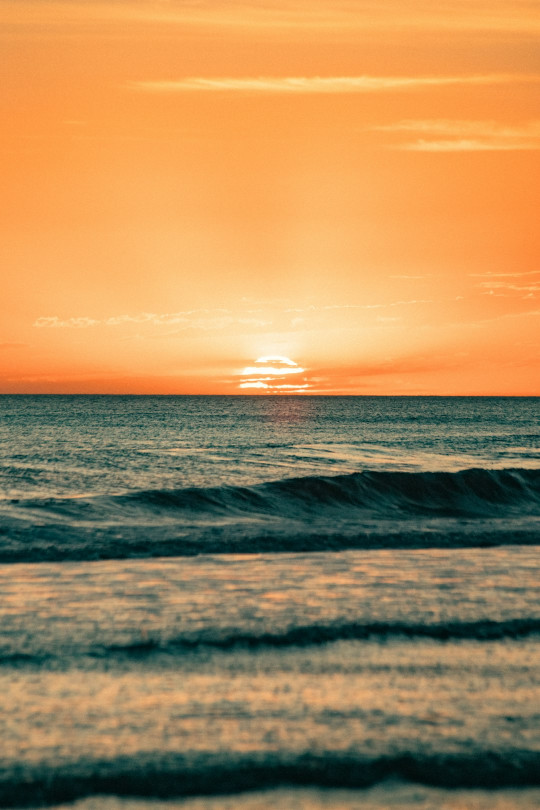 The sun is setting over the ocean with waves