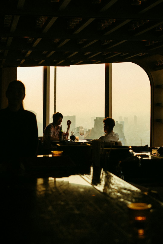 A group of people sitting at a bar with a view of the city