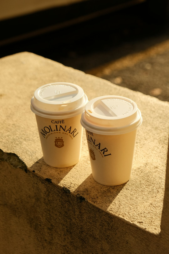 Two cups of coffee sitting on a ledge