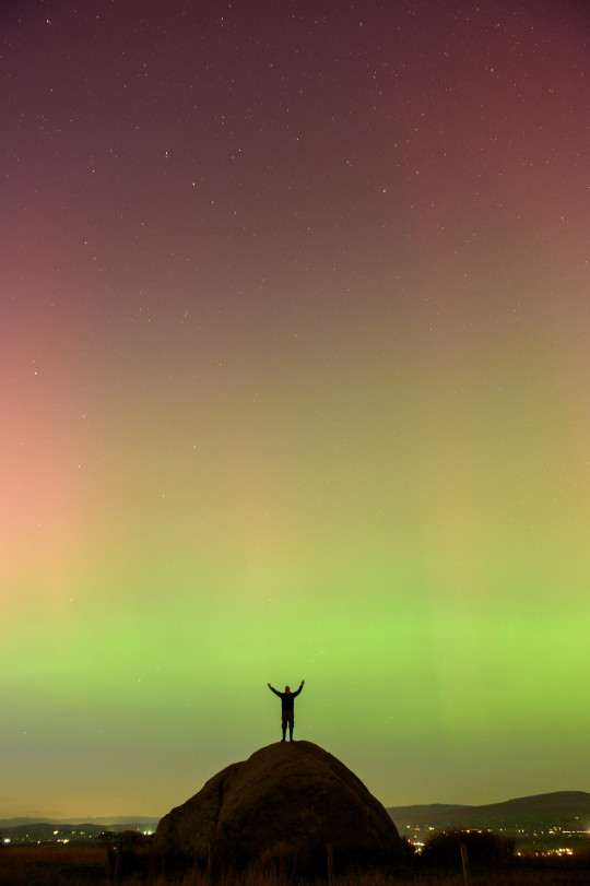 A man standing on top of a hill under a green and pink sky