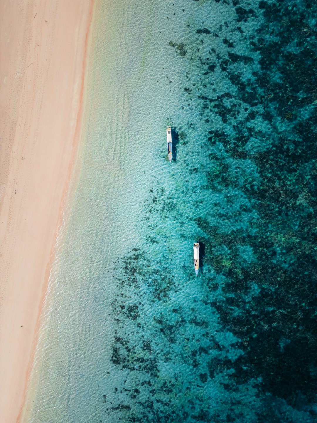 Two boats are in the water near a sandy beach