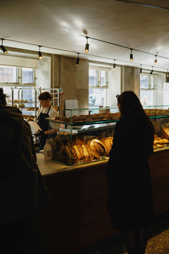 A woman standing in front of a counter filled with bread