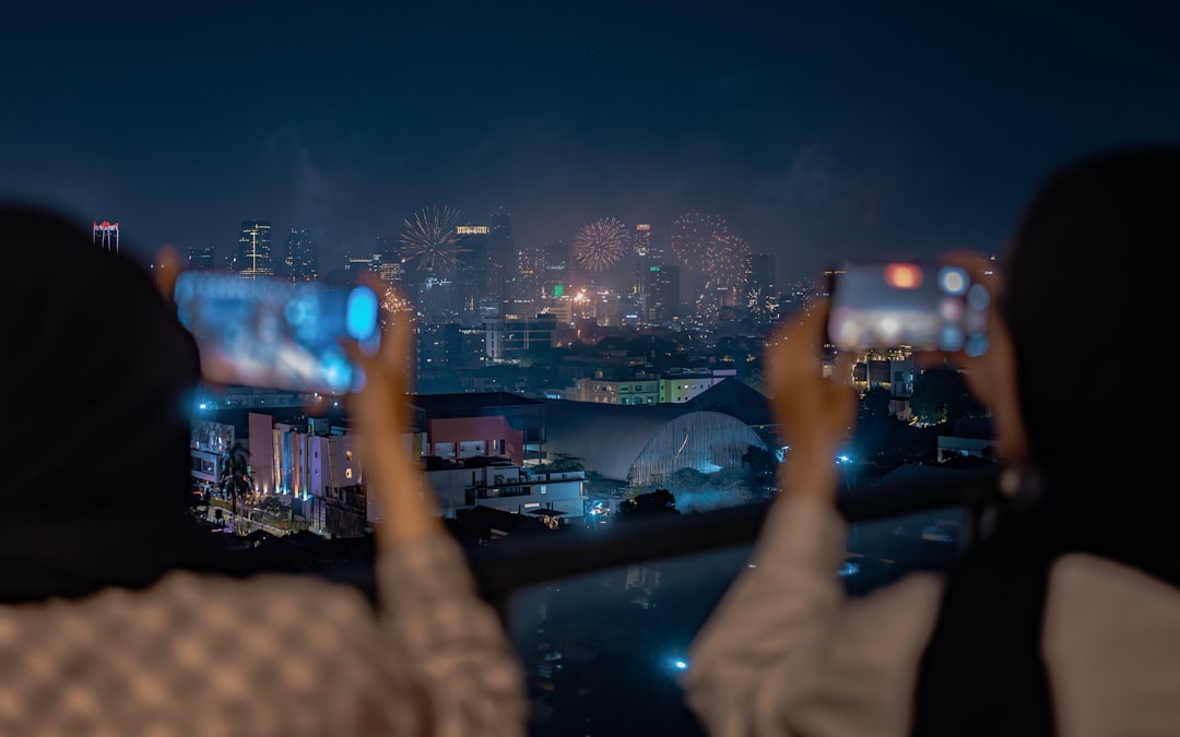 Two people taking pictures of a city at night