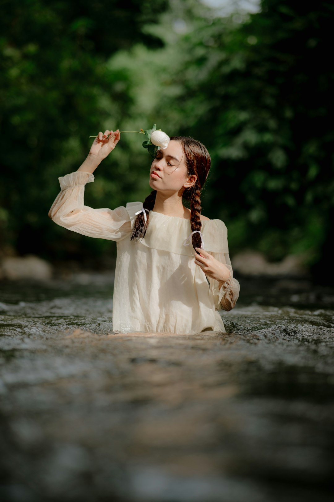 A woman sitting in a river with a flower in her hand