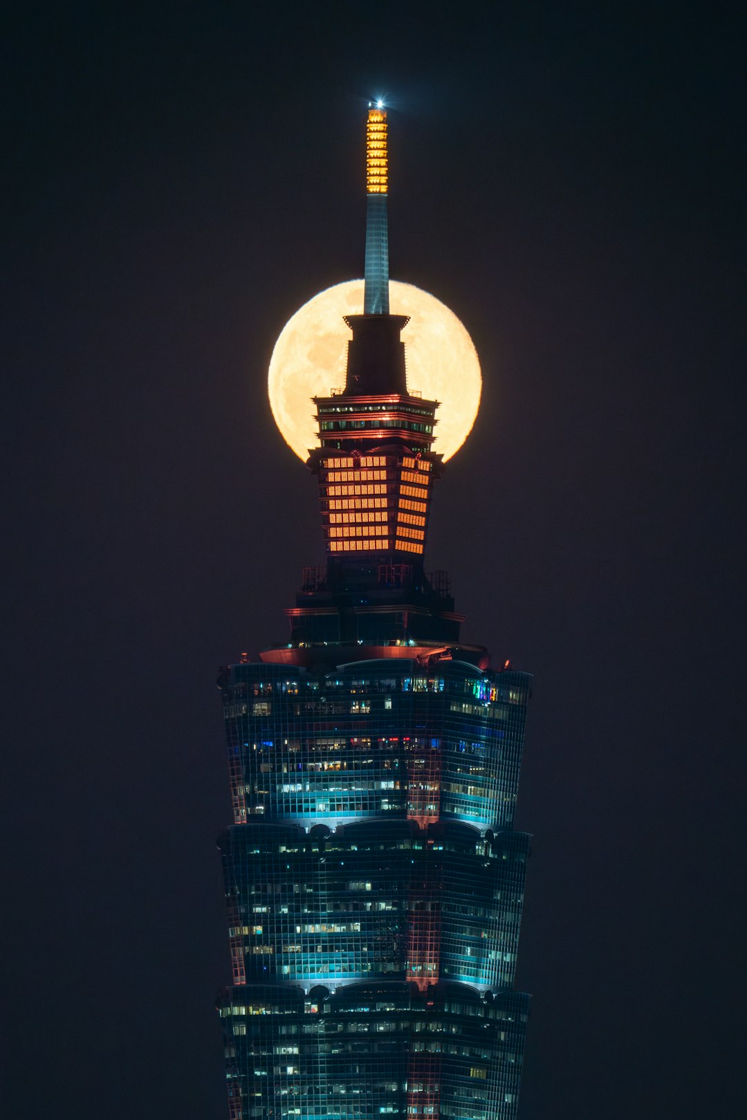 A full moon rises over the top of a skyscraper