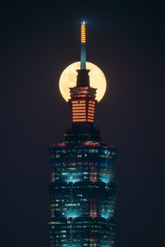 A full moon rises over the top of a skyscraper