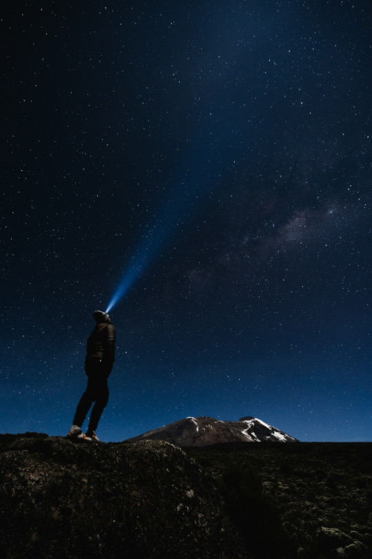 A man standing on top of a mountain under a night sky